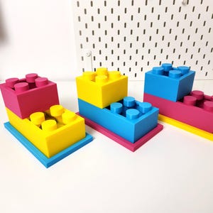 May include: Three sets of colorful plastic building blocks stacked on top of each other. The blocks are yellow, blue, and pink.