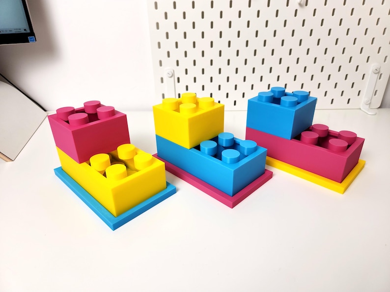 May include: Three sets of colorful plastic building blocks stacked on top of each other. The blocks are yellow, blue, and pink.