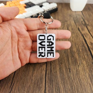 May include: A white keychain with a black pixelated design that says "GAME OVER".