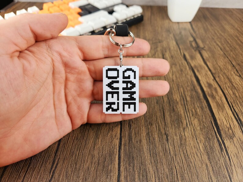May include: A white keychain with a black pixelated design that says "GAME OVER".