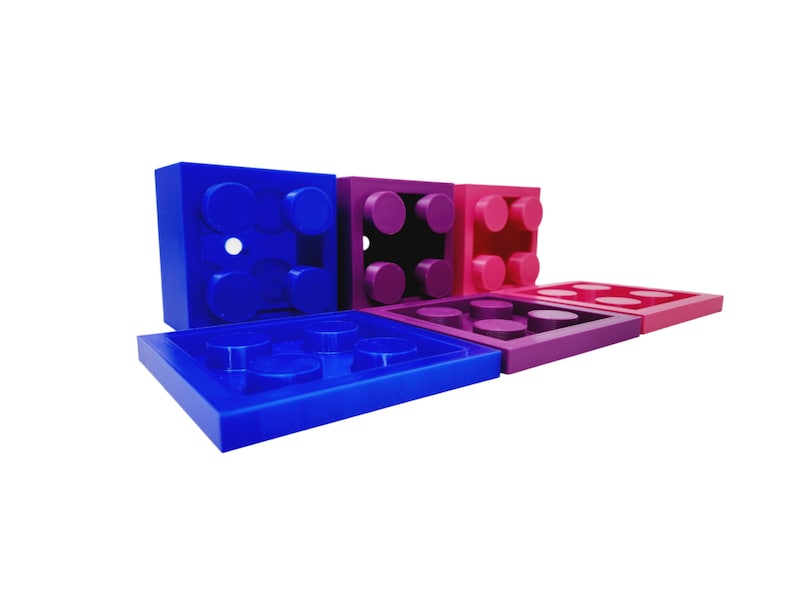 May include: Five plastic building blocks in various shades of blue, purple, and pink. The blocks are arranged in a staggered pattern, with the largest block in the back and the smallest block in the front.