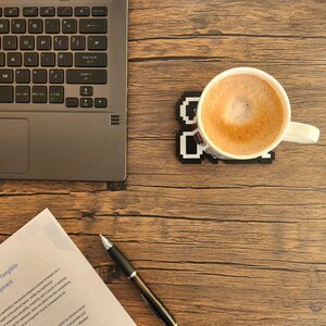 May include: A close-up of a wooden table with a laptop, a cup of coffee, a pen, and a piece of paper with the text "Puzzle Shaped Coaster: A Tangible" and "phor of Utility and Enjoyment".