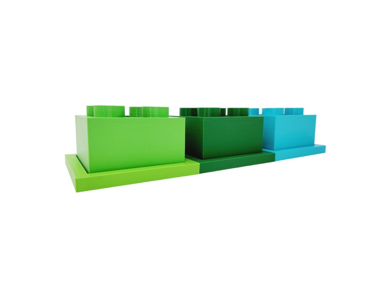 May include: Three green and blue toy building blocks stacked on top of each other. The blocks are made of plastic and have a smooth surface.