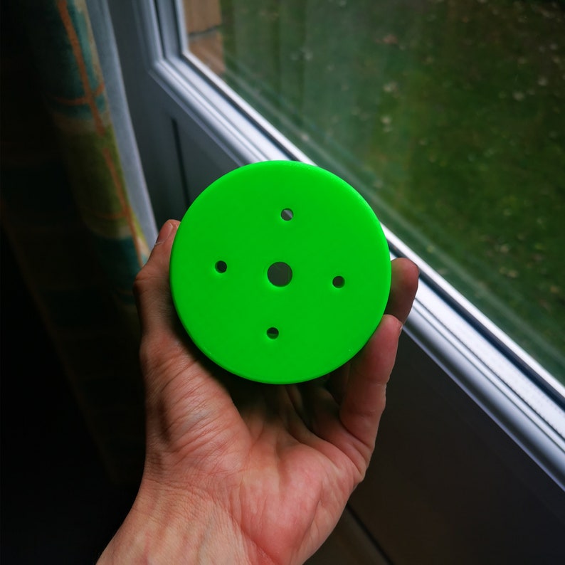 May include: A bright green plastic disc with five holes in it. The disc is being held in a person's hand.