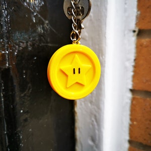 May include: A yellow keychain charm shaped like a star with two small black circles in the center. The charm is attached to a silver key chain.