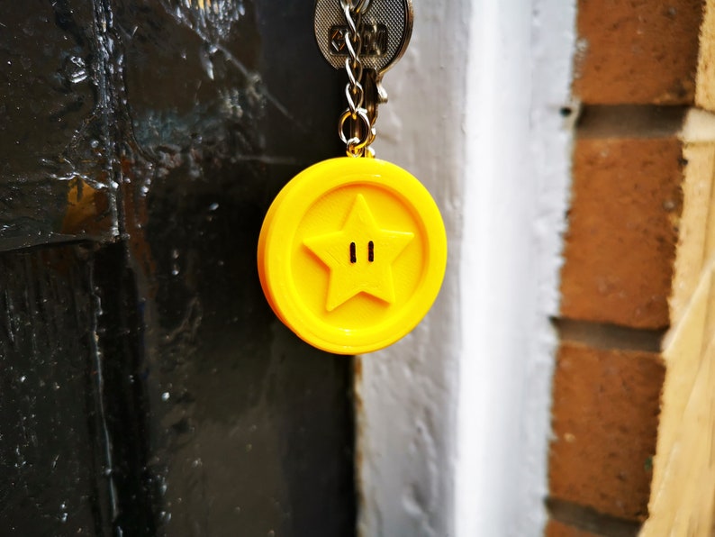 May include: A yellow keychain charm shaped like a star with two small black circles in the center. The charm is attached to a silver key chain.