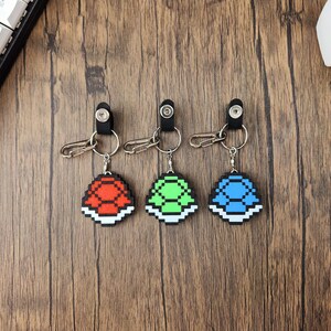 May include: Three keychains featuring pixelated turtle shells in red, green, and blue. Each keychain has a silver ring and a black clip.
