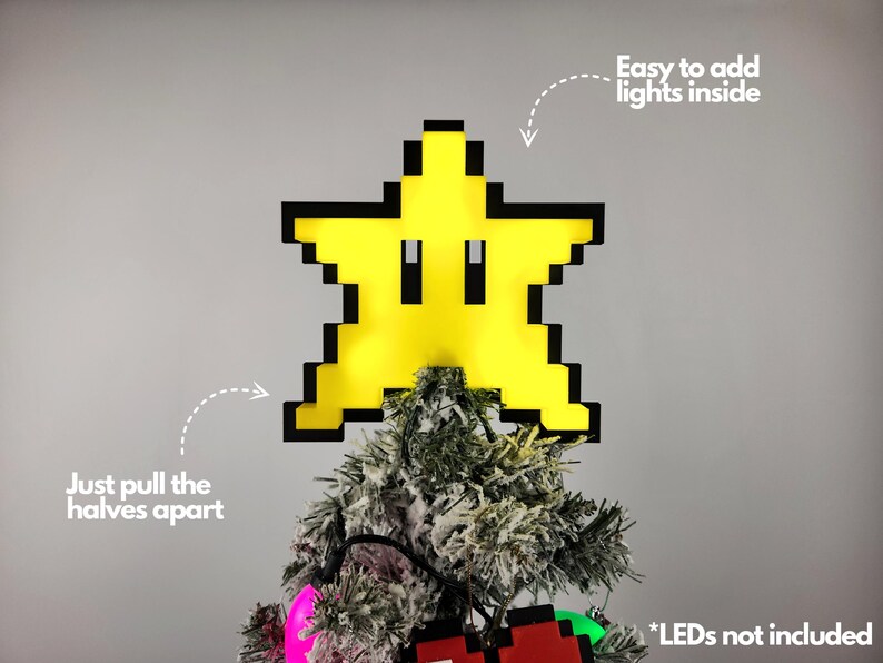 May include: A yellow pixelated star with a black outline, resembling a Super Mario Bros. power-up, is shown on top of a Christmas tree. The star is designed to be a Christmas tree topper and can be opened to add lights inside. The text "Easy to add lights inside" and "Just pull the halves apart" are visible in the image. The text "*LEDs not included" is also visible.