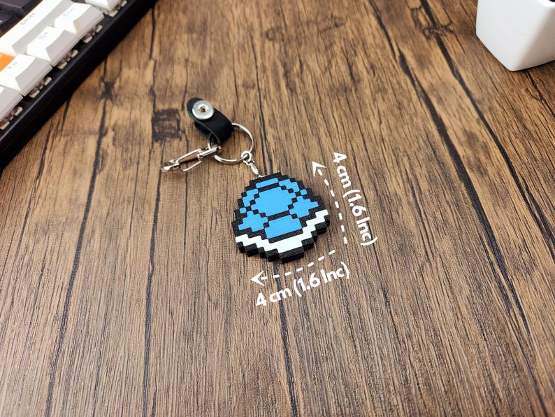 May include: A blue and white pixelated keychain shaped like a turtle shell. The keychain is 4 inches wide and 4 inches tall.