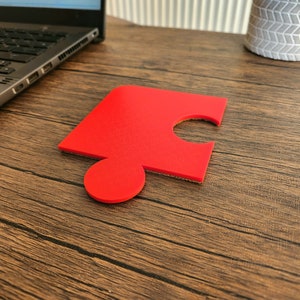 May include: A single red puzzle piece on a wooden surface.