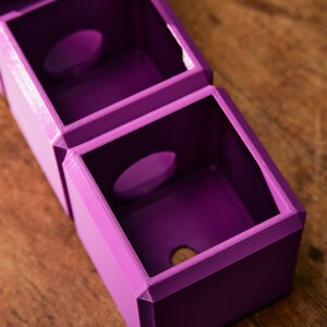 May include: A set of three purple 3D printed boxes with circular openings. The boxes are stacked on top of each other.