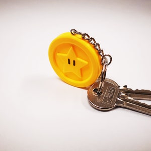 May include: A yellow star-shaped keychain with a black outline and two black dots for eyes. The keychain is attached to two silver keys.