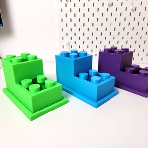 May include: Three different colored plastic toy building blocks stacked on top of each other. The blocks are green, blue, and purple.