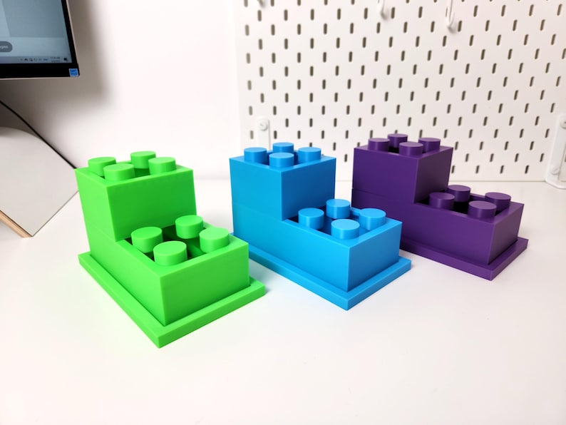 May include: Three different colored plastic toy building blocks stacked on top of each other. The blocks are green, blue, and purple.