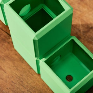 May include: A set of two green, square-shaped planters with a circular opening on the top of each. The planters are stacked on top of each other.