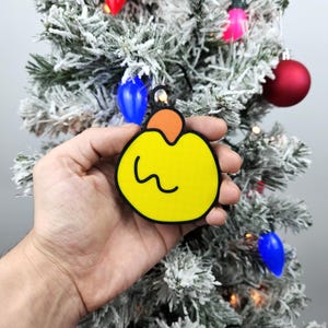 May include: A yellow Christmas ornament with a black outline and a small orange top. The ornament has a wavy line drawn on the front.