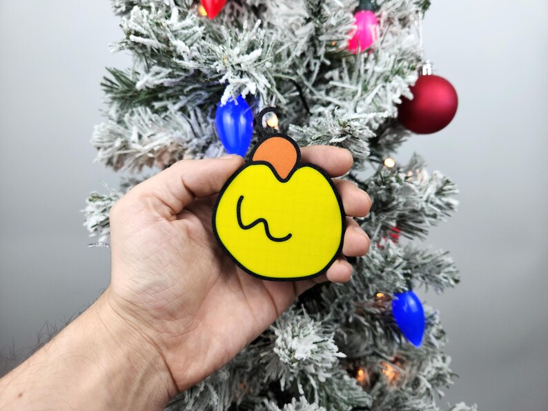 May include: A yellow Christmas ornament with a black outline and a small orange top. The ornament has a wavy line drawn on the front.