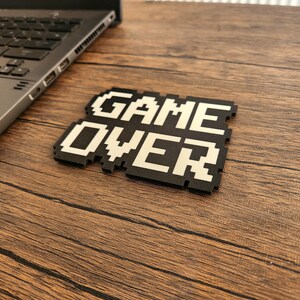 May include: A black and white pixelated game over sign on a wooden surface.