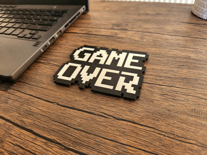 May include: A black and white pixelated game over sign on a wooden surface.