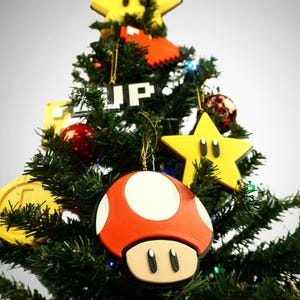 Puede incluir: Un &aacute;rbol de Navidad decorado con adornos rojos y amarillos, incluyendo un hongo rojo y blanco, una estrella amarilla con una cara y una moneda amarilla. El &aacute;rbol est&aacute; decorado con la palabra "UP" en letras de bloque.