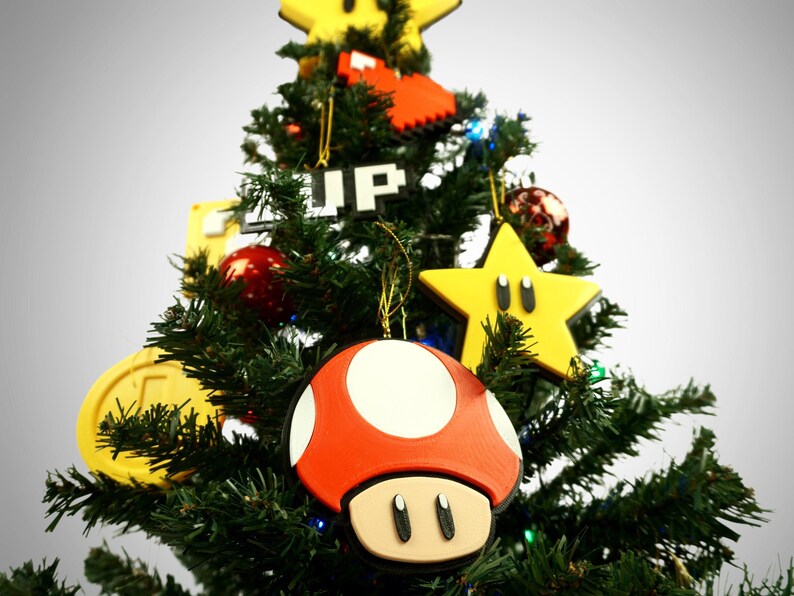Puede incluir: Un &aacute;rbol de Navidad decorado con adornos rojos y amarillos, incluyendo un hongo rojo y blanco, una estrella amarilla con una cara y una moneda amarilla. El &aacute;rbol est&aacute; decorado con la palabra "UP" en letras de bloque.