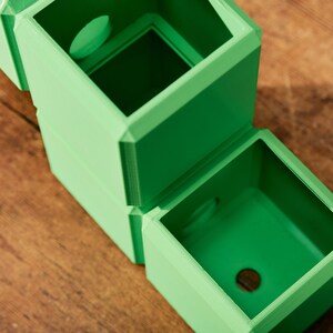 May include: A set of two green, square-shaped planters with a circular opening on the top of each. The planters are stacked on top of each other.