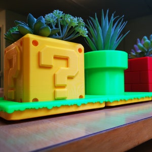 May include: Three yellow, green, and red plant pots with a question mark on the yellow pot. The pots are on a wooden surface.