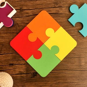 May include: Four colorful puzzle pieces fit together to form a square shape on a wooden surface. The pieces are red, orange, yellow, and green.