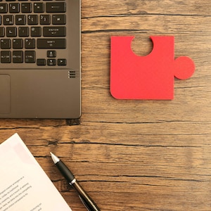 May include: A red puzzle piece on a wooden surface. A laptop, a pen, and a piece of paper with the text "Coaster: A Tangible" are also visible.