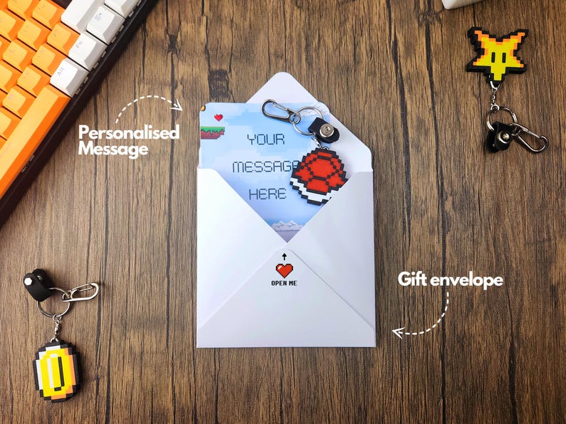 May include: A white envelope with a red heart and the text "Open Me" on the front. The envelope contains a card with a pixelated image of a turtle shell and the text "Your message here". The envelope is accompanied by a keychain with a pixelated image of a gold coin and a pixelated image of a star.
