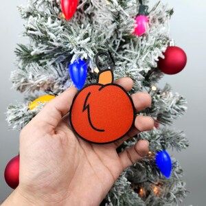 May include: A hand holds a red and orange Christmas ornament shaped like a pumpkin. The ornament has a black outline and a black lightning bolt design.