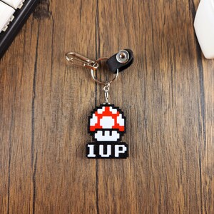May include: A black and white pixelated mushroom keychain with the word "1UP" on the bottom. The keychain is attached to a silver key ring and a black leather loop.