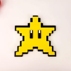May include: A yellow pixelated star with black outlines and two black eyes. The star is a 3D printed object.