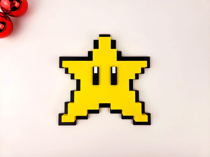 May include: A yellow pixelated star with black outlines and two black eyes. The star is a 3D printed object.