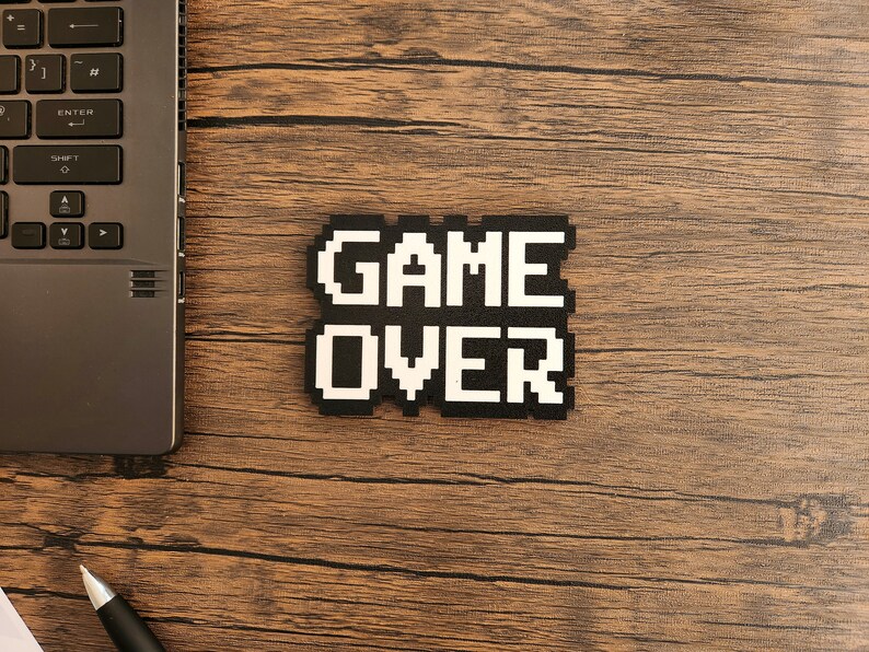 May include: A black and white pixelated sign that reads "GAME OVER" on a wooden surface.