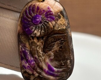 May include: A carved purple and brown stone pendant with a flower design. The pendant is attached to a gold chain.