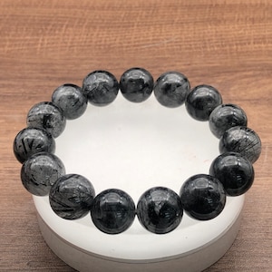 Op de afbeelding: Een zwarte armband gemaakt van ronde, gladde, zwarte en grijze edelsteen kralen. De kralen hebben een uniek, marmerpatroon.