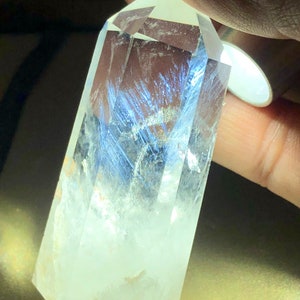 Może przedstawiać: Szpiczasty kryształ kwarcu o przezroczystym kolorze z niebieskim wtrąceniem fantomowym. Kryształ jest fasetowany i ma ostry czubek.