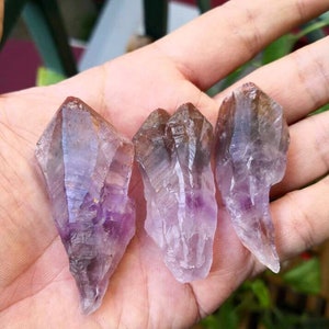 May include: Three amethyst crystals with a purple and brown color. The crystals are pointed and have a natural, rough texture.