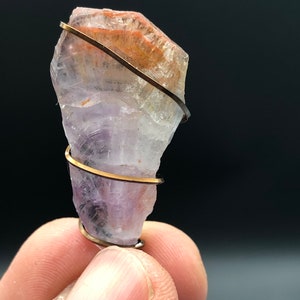May include: A purple, orange, and clear amethyst crystal wrapped in gold wire.