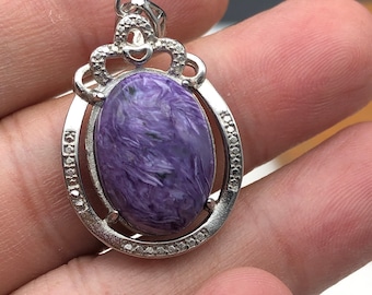 May include: A silver pendant with a purple and black stone set in an oval shape. The pendant has a decorative bail with a swirl design.
