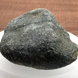 Puede incluir: Una roca redonda y lisa de color gris oscuro con una superficie ligeramente texturizada.