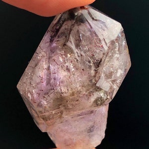 May include: A clear, faceted crystal with a purple hue and red inclusions. The crystal is shaped like a double-terminated point.