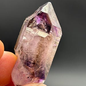 May include: A clear amethyst crystal with purple and white hues. The crystal is double terminated and has a pointed shape.