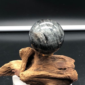 May include: A black and white gemstone sphere on a wooden stand. The sphere has a smooth, polished surface and a swirling pattern of black and white.