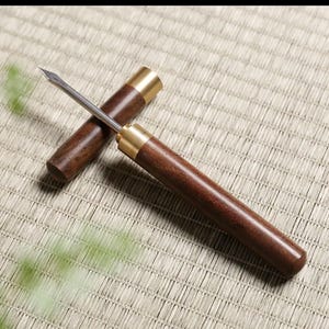 May include: A tea needle with a dark wood handle and a brass ferrule. The needle is made of stainless steel. The tea tool is used to loosen compressed tea leaves. The needle is 5.5 inches long.