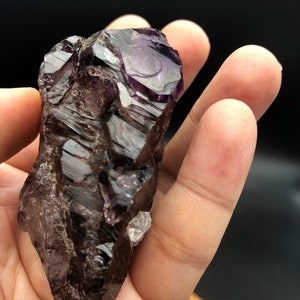 May include: A large, dark purple amethyst crystal with a pointed tip and a rough, textured surface. The crystal has a deep, rich color and is partially translucent.