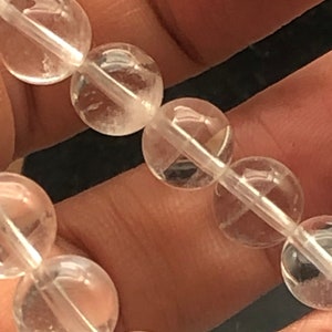 May include: A close-up of a clear quartz crystal bracelet with round beads. The bracelet is made of natural stones and is strung on a clear elastic cord.