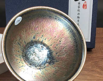Puede incluir: Una taza de té de cerámica marrón oscuro con un esmalte iridiscente único. El esmalte tiene un efecto craquelado con un tono plateado y rosado. La taza tiene el número "3" escrito en el lateral.
