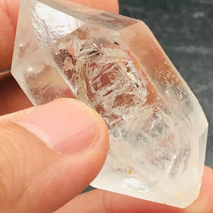 May include: A clear quartz crystal with a double-terminated point, also known as a double-pointed crystal. The crystal has a natural, raw appearance with inclusions and striations.